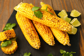 Board with tasty grilled corn cobs and lime on wooden background