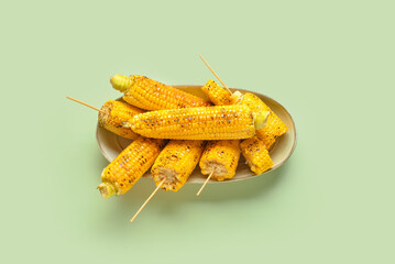 Bowl with tasty grilled corn cobs on green background