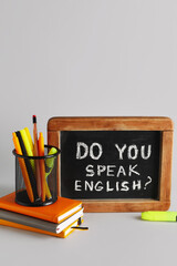 Stationery and blackboard with question DO YOU SPEAK ENGLISH? on grey background