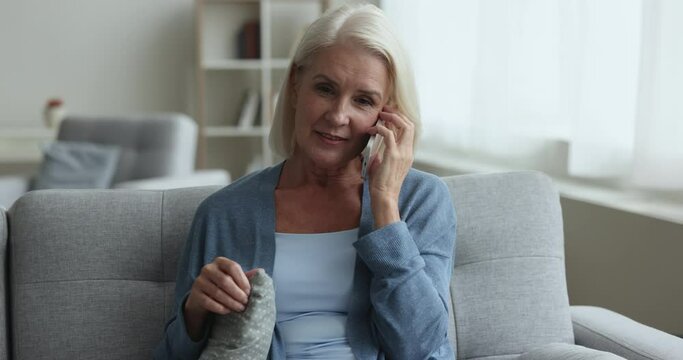Positive relaxed senior woman talking on mobile phone at home, resting on cozy home couch, looking away, speaking on cellphone, enjoying telephone call, wireless communication