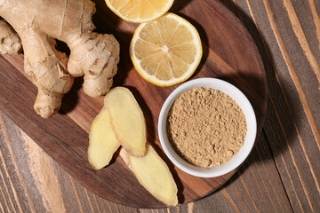 Board with fresh ginger root, lemon and bowl of dried powder on wooden background