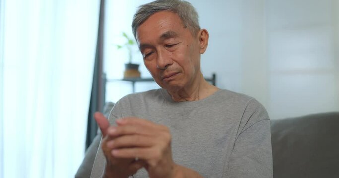Asian senior man has tingling and numbness in his hand which causes beriberi. Mature asian man with wrist pain at home.
