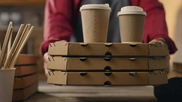 Fast food restaurant, Operator waiter issues orders for ready coffee and hot pizza, Receiving an order by a client, Fast food preparation shop operator in special uniform holds boxes pizza and coffee