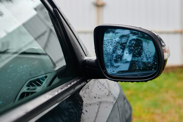 Right black wing mirror of modern car. Car side rear-view mirror with water drops.