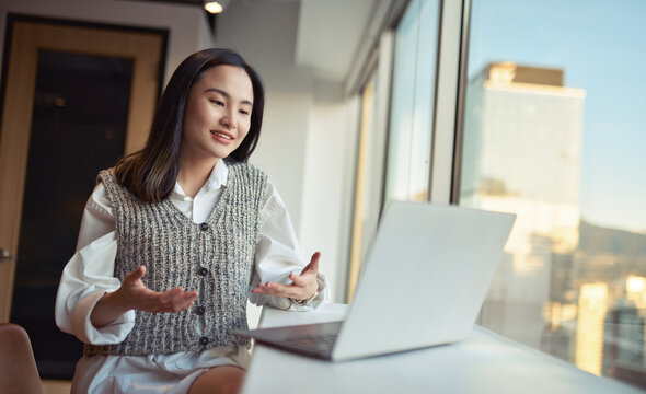 Young happy Asian woman professional executive or hr manager having hybrid video conference call online work meeting managing team communicating by videocall working on laptop in modern office.
