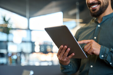 Smiling young business man holding pad computer in hands at work. Male professional employee using digital tablet fintech device standing in office checking financial market data. Close up, copy space - Powered by Adobe