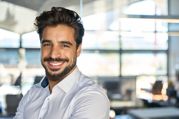 Happy young Latin business man standing in office, headshot close up portrait. Smiling Hispanic...