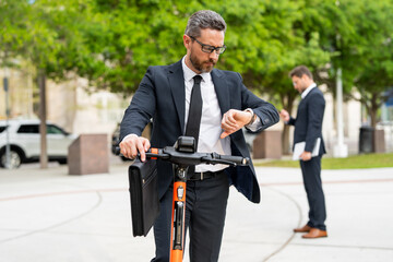 Attractive business man riding a kick scooter at New York park. Business man in a suit riding an electric scooter on a business meeting. Middle aged business man riding scooter in suit.