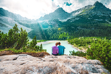 Fototapeta na wymiar Young sportive couple enjoys view on the turquoise Sorapis lake from a beautiful restpoint in the afternoon. Lake Sorapis, Dolomites, Belluno, Italy, Europe.