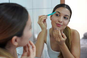 Facial hair removal. Close-up of beautiful young woman shaving her face by razor at home.