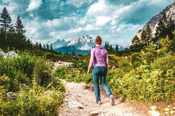 Naklejka premium Athletic woman walks on hiking trail at Sorapis lake with impressive view on Cadini di Misurina in the background in the evening. Lake Sorapis, Dolomites, Belluno, Italy, Europe.