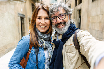 Portrait of senior attractive couple smiling at camera at city street. Mature people taking self portrait on summer vacation.