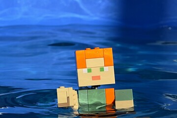 Obraz premium LEGO Minecraft large action figure of Alex is swimming in deep blue water of summer swimming pool. 