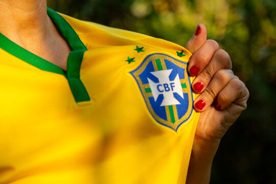 Detalhe na m&atilde;o de uma mulher com unhas vermelhas, mostrando o escudo da sele&ccedil;&atilde;o brasileira de sua camisa.