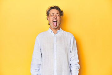 Middle-aged man posing on a yellow backdrop funny and friendly sticking out tongue.