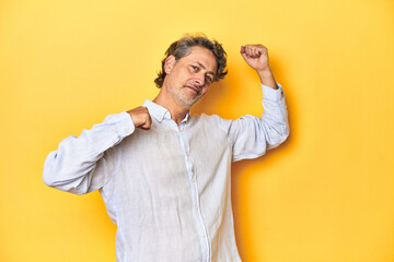 Middle-aged man posing on a yellow backdrop celebrating a special day, jumps and raise arms with energy.