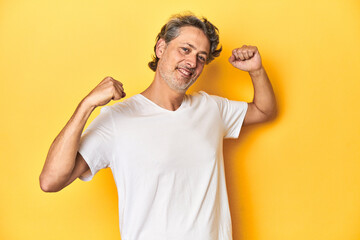 Middle-aged man posing on a yellow backdrop celebrating a special day, jumps and raise arms with energy.