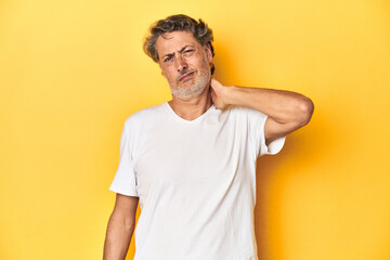 Fototapeta na wymiar Middle-aged man posing on a yellow backdrop having a neck pain due to stress, massaging and touching it with hand.