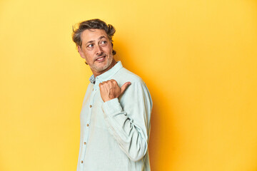 Fototapeta premium Middle-aged man posing on a yellow backdrop points with thumb finger away, laughing and carefree.