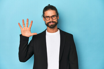 Businessman in suit with eyeglasses and beard smiling cheerful showing number five with fingers.