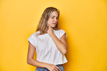 Young blonde Caucasian woman in a white t-shirt on a yellow studio background, suffers pain in...