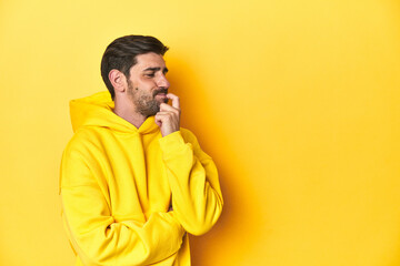Fototapeta premium Man in yellow hoodie, monochrome studio backdrop relaxed thinking about something looking at a copy space.