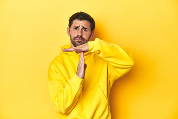 Man in yellow hoodie, monochrome studio backdrop showing a timeout gesture.