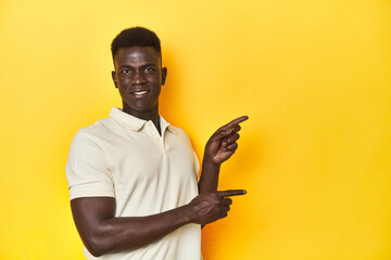 Stylish young African man on vibrant yellow studio background, shocked pointing with index fingers...