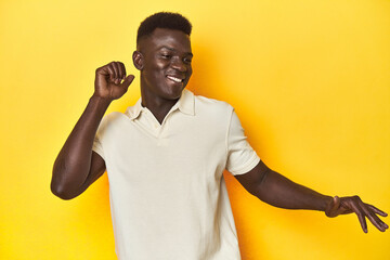 Stylish young African man on vibrant yellow studio background, dancing and having fun.