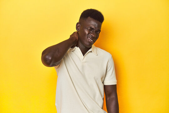 Stylish young African man on vibrant yellow studio background, suffering neck pain due to sedentary lifestyle.