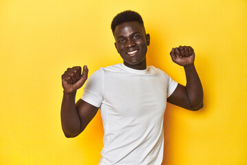 Stylish young African man on vibrant yellow studio background, dancing and having fun.