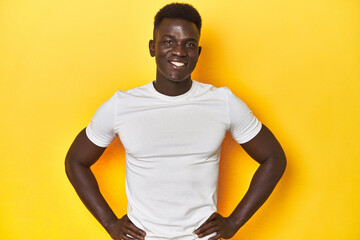 Stylish young African man on vibrant yellow studio background, confident keeping hands on hips.