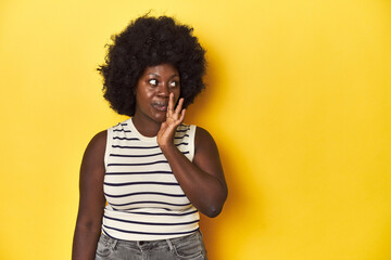 Fototapeta na wymiar African-American woman with afro, studio yellow background is saying a secret hot braking news and looking aside