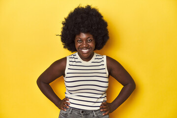 Fototapeta na wymiar African-American woman with afro, studio yellow background confident keeping hands on hips.