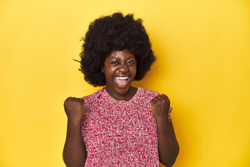 African-American woman with afro, studio yellow background cheering carefree and excited. Victory concept.