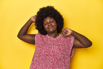 African-American woman with afro, studio yellow background celebrating a special day, jumps and...