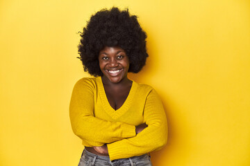 Fototapeta na wymiar African-American woman with afro, studio yellow background who feels confident, crossing arms with determination.