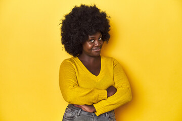 African-American woman with afro, studio yellow background suspicious, uncertain, examining you.