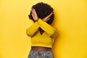African-American woman with afro, studio yellow background keeping two arms crossed, denial concept.
