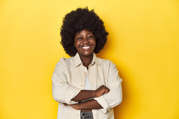 African-American woman with afro, studio yellow background who feels confident, crossing arms with determination.