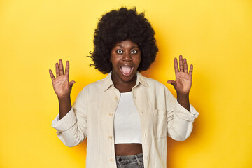 African-American woman with afro, studio yellow background receiving a pleasant surprise, excited...