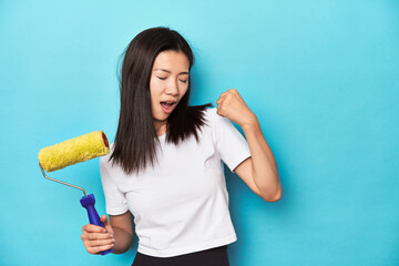 Young Asian woman with paint roller, DIY concept, raising fist after a victory, winner concept.