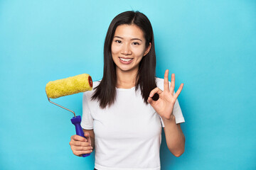 Young Asian woman with paint roller, DIY concept, cheerful and confident showing ok gesture.