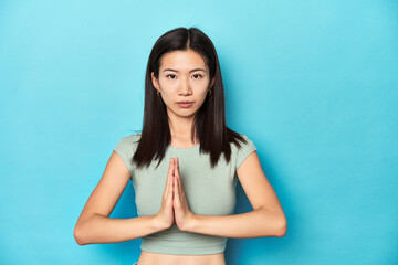 Asian woman in summer green top, studio backdrop, praying, showing devotion, religious person looking for divine inspiration.