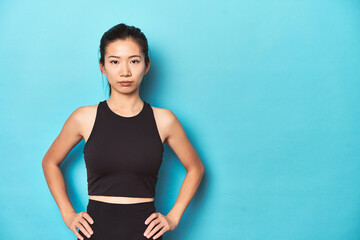 Fototapeta na wymiar Young Asian sportswoman, studio shot, on blue background.