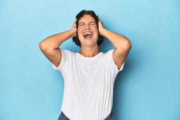 Young Caucasian woman with short hair laughs joyfully keeping hands on head. Happiness concept.