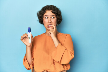 Young woman holding pregnancy test, studio background relaxed thinking about something looking at a copy space. © Asier