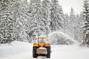 A snowplow truck clearing a snow-covered road in the European Alps while a snowstorm. Drifts and...