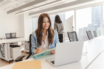 Smiling american woman using laptop, having video call while sitting in modern office