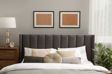 Comfortable bed with cushions, lamp and different decor on wooden chest of drawers in room. Stylish...